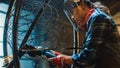 Close Up of Young Female Fabricator in Safety Mask. She is Grinding a Metal Tube Sculpture with an