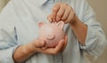 Depositing money in a piggy bank on wooden table at home. Saving money for future plan and retirement fund concept.