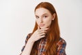 Close-up of young female student with red natural hair, pale skin and blue eyes, looking thoughtful at camera, making Royalty Free Stock Photo