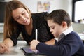 Close up of young female teacher sitting at desk with a Down syndrome schoolboy using a tablet computer in a primary school classr Royalty Free Stock Photo