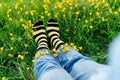 Close up young female wearing jeans and striped black and yellow socks with flowers inside sitting on the green grass of
