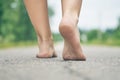 Young girl`s bare feet walking along asphalt road close up. Rear view Royalty Free Stock Photo