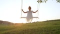 CLOSE UP Young girl swinging on wooden swing in a green meadow at summer sunset