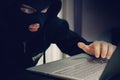 Close up of a young hacker in black mask and hood sits at the laptop screen. Internet criminal scans user`s information. Cyber