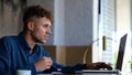 Close up of young handsome man sitting in restaurant and eating meal while typing on laptop. Remote work. Caucasian male Royalty Free Stock Photo