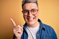 Close up of young handsome modern man wearing glasses and denim jacket over yellow background very happy pointing with hand and Royalty Free Stock Photo