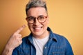 Close up of young handsome modern man wearing glasses and denim jacket over yellow background very happy pointing with hand and Royalty Free Stock Photo