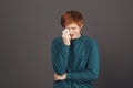 Close up of young handsome sensitive ginger teenager in green sweater crying, wipes tears with paper napkin, being tired Royalty Free Stock Photo