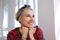 Close-up of young happy blonde in headband leaning her face on raised hands and smiling cheerfully, being in nice mood while