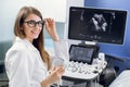 Close up of young happy female doctor in white coat posing to camera with smile while sitting near ultra ultrasound Royalty Free Stock Photo