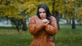 Close-up young hispanic woman standing in autumn park outdoors girl frozen shivering from cold trying to keep warm with