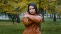 Close-up young hispanic woman standing in autumn park outdoors girl frozen shivering from cold trying to keep warm with