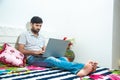 Close up of Young indian man busy working on his laptop doing office work while relaxing on bed in bedroom, freelancer working Royalty Free Stock Photo