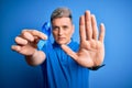 Close up of young man holding colon cancer awareness blue ribbon over isolated background with open hand doing stop sign with Royalty Free Stock Photo