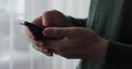 Close up young man holding mobile phone in hands texting message in web chat surfing, reading news. Man work online