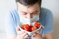 Close up Young Man in medical mask holding bowl with strawberry. man in an anti-virus medical mask . recovery from
