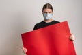 Close up of a young man with protective mask against virus epidemy is holding an empty red cardboard against white