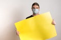 Close up of a young man with protective mask against virus epidemy is holding an empty yellow cardboard against white
