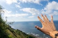 Close-up of a young man`s hand on seascape, with blue sky and white clouds