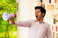 Close up of a young man shouting with a megaphone, with his arm stretched in a blurred background