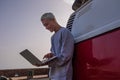 Close up of young man using his laptop and computer alone at the evening with on his back a red and white minivan - nomad Royalty Free Stock Photo