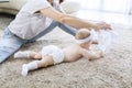 Young mother dressing her cute baby on carpet