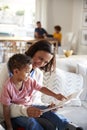 Close up of young mother sitting on a sofa in the living room reading a book with her toddler son, sitting on her knee, father and Royalty Free Stock Photo