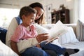Close up of young mother sitting on a sofa in the living room reading a book with her toddler son, who is sitting on her knee, sid Royalty Free Stock Photo
