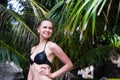 Close-up of young slim girl standing on a beach wearing black bikini swimwear with green palm leaf on the Royalty Free Stock Photo