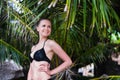 Close-up of young slim girl standing on a beach wearing black bikini swimwear with green palm leaf on the Royalty Free Stock Photo