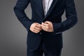 Close up of a young slim business man in blue suit on grey background adjust the button of his jacket with both hands Royalty Free Stock Photo