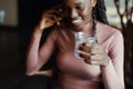 Close-up of young smiling cute African-American woman sitting at beige table, holding glass of water, looking aside. Royalty Free Stock Photo