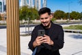 Close-up of young smiling Latino checking and answering messages with his cell phone or smart phone in a public square. Concept Royalty Free Stock Photo