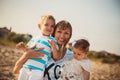 Close up of young smiling mother hugging her small kids, having fun at beach together, happy lifestyle family concept. Royalty Free Stock Photo