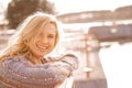 Close-up of young smiling woman with long wavy fair hair wearing brown cardigan, standing at concrete river embankment. Royalty Free Stock Photo