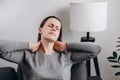 Close up young unhappy caucasian woman sitting on couch holding hands on neck, suffering from neck pain, incorrect posture, joint