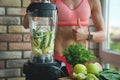 Close up of young woman with blender and green vegetables making detox shake or smoothie at home