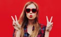 Close up of young woman blowing red lips sending sweet air kiss wearing a red heart shaped sunglasses over background Royalty Free Stock Photo