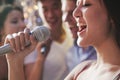 Close- up of young woman holding a microphone and singing at karaoke, friends singing in the background Royalty Free Stock Photo