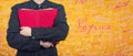 Woman holding a red book to chest. Education concept as student hugging a textbook, loving knowledge isolated over yellow wall Royalty Free Stock Photo