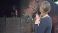 Close up of young woman kissing her horse before riding. Close up of brown horse eating while woman holding by the