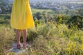 Close up of young woman legs in yellow summer dress standing in grassy field outdoors Royalty Free Stock Photo