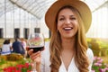 Close-up of young woman looking at camera and holding glass of wine with people among flowers field drinking and chatting on the Royalty Free Stock Photo