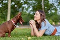 Close-up of young woman lying on green grass with her little dog, Pharaoh hound breed puppy, outdoors, in a park. Royalty Free Stock Photo