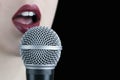 Close up of a young woman with red lips singing to the microphone isolated on black background Royalty Free Stock Photo