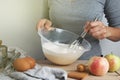 Close-up young woman`s hands holding whisk and bowl while making pie, cake. Female cooking dough for pie on wooden table Royalty Free Stock Photo