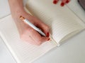 Close-up of a young woman`s hands writing a plan of the day in a notebook at the workplace at the computer. Royalty Free Stock Photo