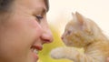 CLOSE UP: Young woman smiles as she lifts a cute orange cat up to her face. Royalty Free Stock Photo