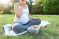 Close-up of young woman in sport clothing sitting on exercise mat and eating fresh apple during training outdoors. Expecting