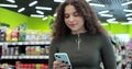 Close up young woman use smartphone in supermarket. Woman buyer using mobile phone application standing with shopping Royalty Free Stock Photo